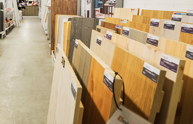 Butiksgång med ställ av ljusa och mörka trägolvprover mot betonggolv