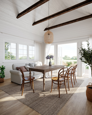 Ljust matsalsrum med vita väggar, synliga träbalkar, träbord med stolar, soffa och gröna växter.