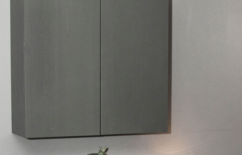 Grått väggskåp i träfinish mot ljusgrå vägg, med grön krukväxt under.