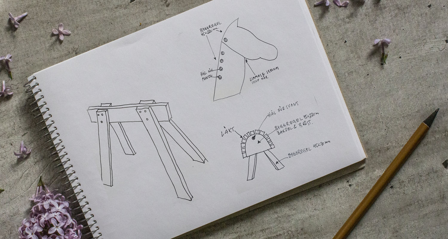 Vit skissbok med svarta penndrag av träbock och hästhuvud, lila syrén på grått bord