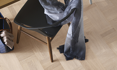 Svart stol med träben, grå sjal slängd över, blå väska med beige tyg på parkettgolv.