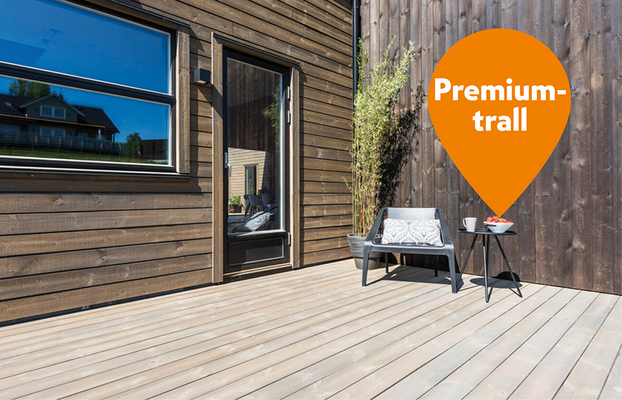 Ljusgrå trall vid mörk träfasad med grå stol och bord med mugg samt orange Premium-trall-bubbla