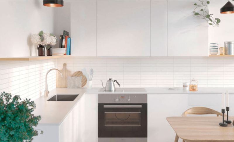 Modernt vitt kök med svart inbyggnadsugn, trädetaljer, gröna växter och hängande lampor.