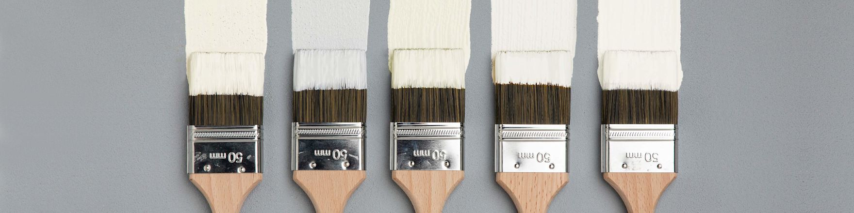 Fem träpenslar med 50 mm metallfäste doppade i vit färg på ljusgrå bakgrund.