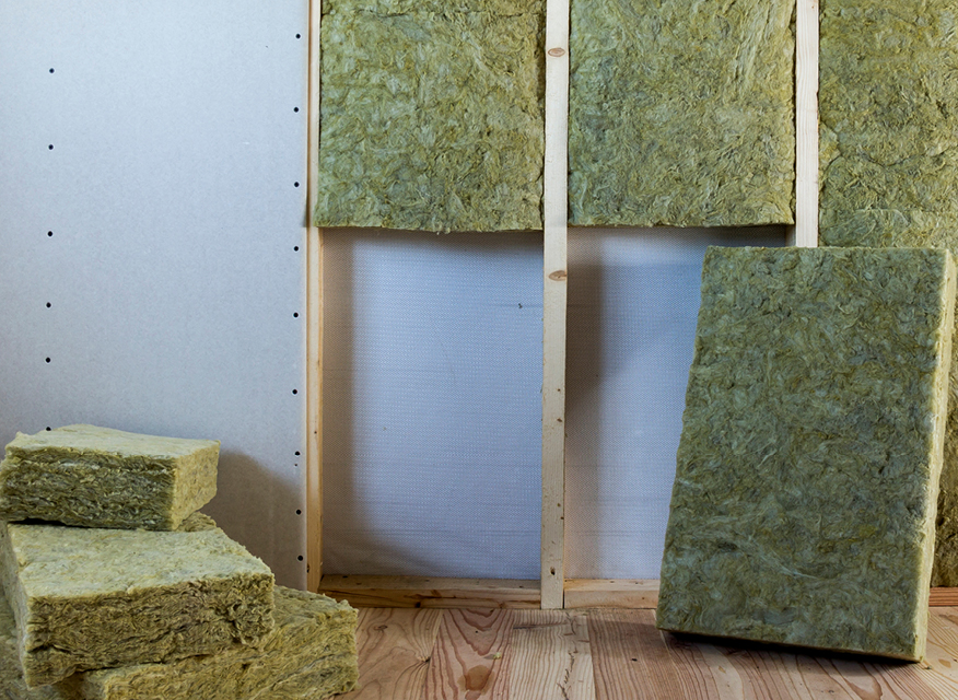 En vägg med träreglar där isoleringsskivor av mineralull är monterade, med fler skivor staplade på golvet.