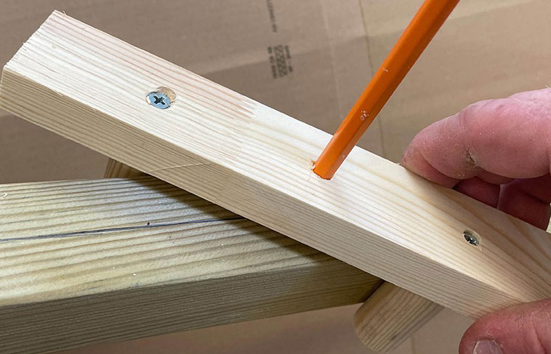 Hand håller hopskruvade ljusa träbitar, en orange blyertspenna markerar ett märke.