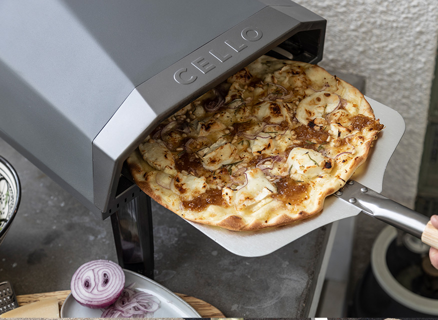 Grå Cello-pizzaugn på utebord med tunn pizza toppad med ost, karamelliserad lök och rödlök