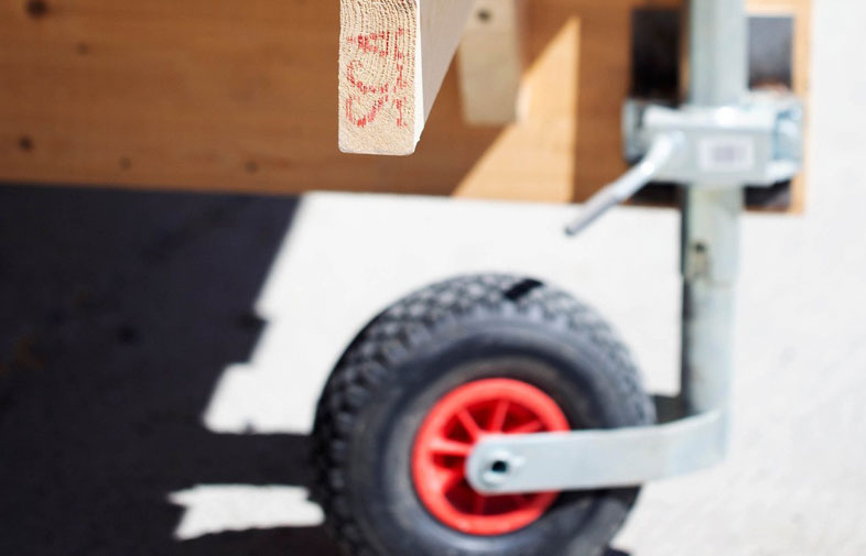 Närbild på hjul med svart däck och röd nav på silverfärgad stödarm under träram.