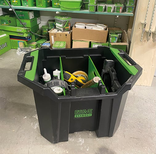 Svart Essbox med gröna insatser fylld med verktyg framför hylla med gröna förpackningar.