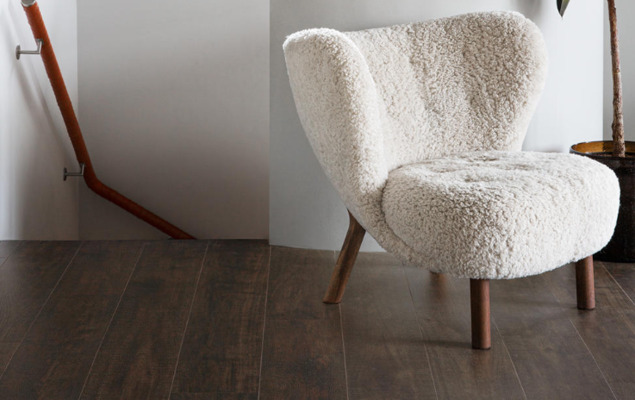 Vit lurvig fåtölj på mörkt trägolv vid vit vägg och trähandledare vid trappa.