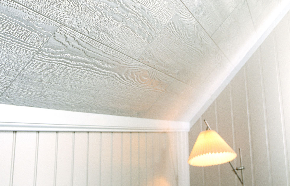 Snedtak i vitt trä med tydlig ådring, beige väggpanel och varm gul golvlampa.