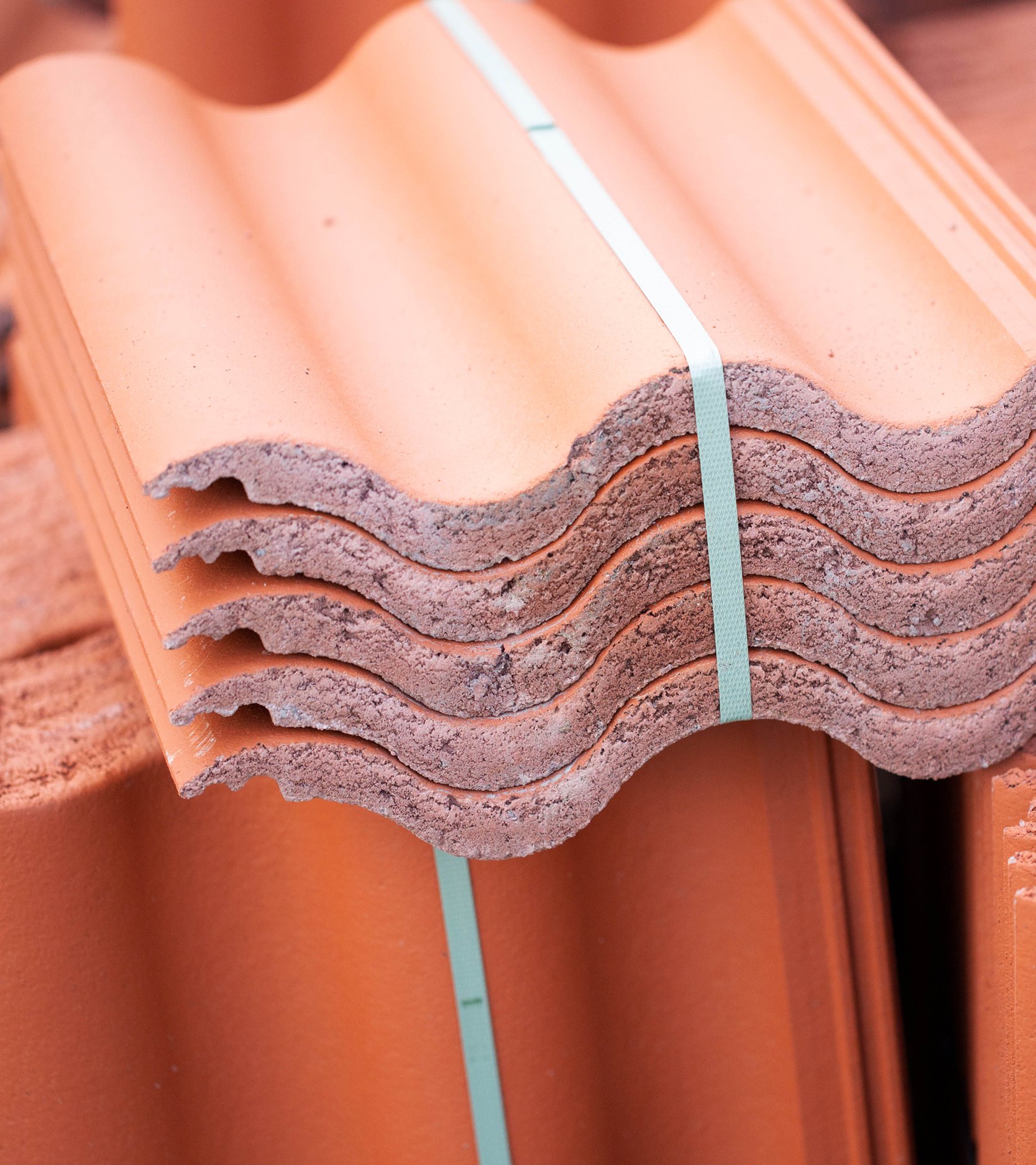 Stapel med terrakottafärgade, vågformade takpannor bundna med grön rem.