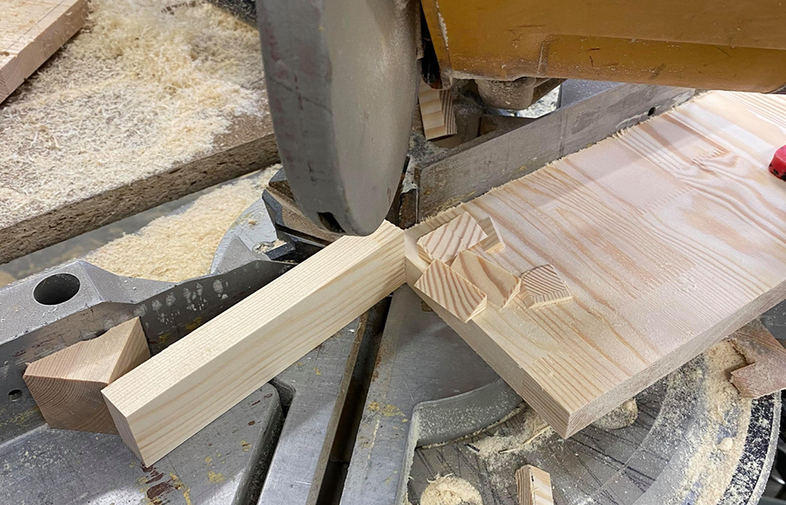 Gul kapsåg skär ljus träplanka på grå metallbas, träspån och träbitar runtom.