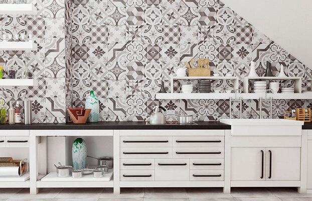 Vit köksbänk med svarta handtag, mönstrad gråvit kakelvägg och öppna hyllor med köksredskap.