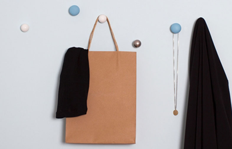 Ljusgrå vägg med blå, vita och silverknoppar, brun kasse med svart tyg, svart plagg och halsband.