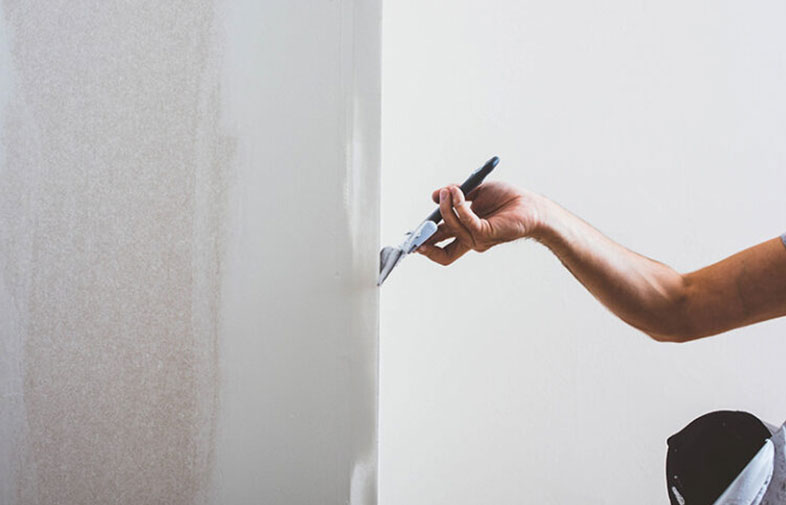 En kortärmad arm målar en ljusbeige vägg vit med pensel