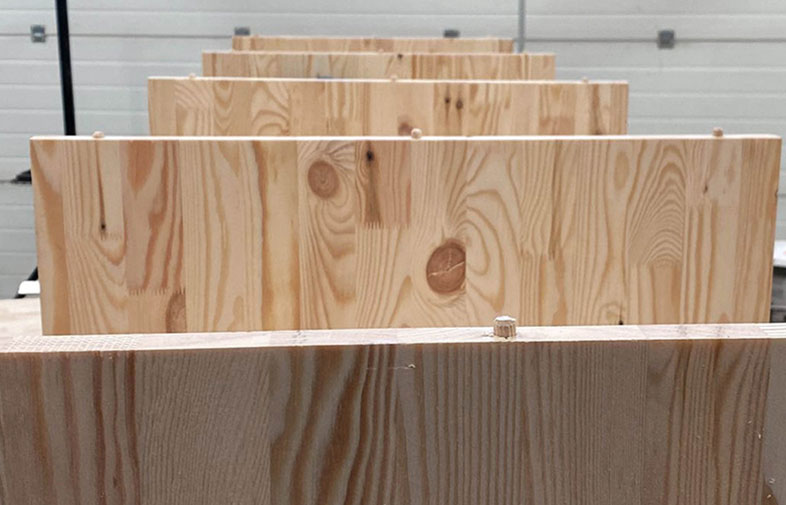 Rader av ljusa furubräddor med synliga kvistar i ljus verkstadsmiljö.