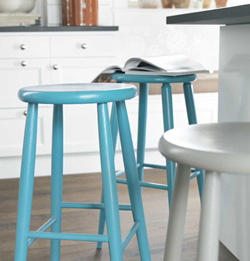 Tre barstolar i kök: två turkosa, en vit, med uppslagen bok på en turkos stol.