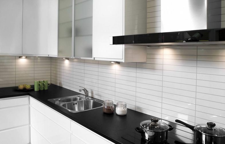 Modernt vitt kök med svart bänkskiva, diskho, glasburkar, kastruller och gröna muggar