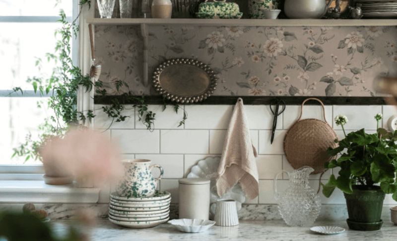 Marmorbänk med vita kakelplattor, blommig tapet, porslin, grön krukväxt och rottingkorg.