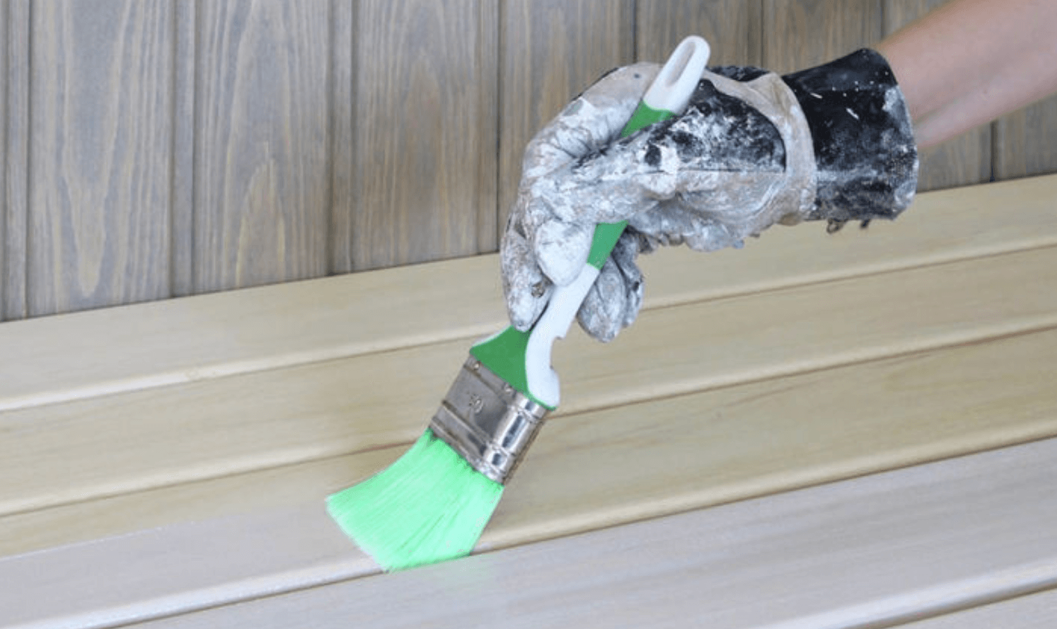 Närbild på målarhandske som sveper en pensel med knallgrön borste över ljust träpanel.