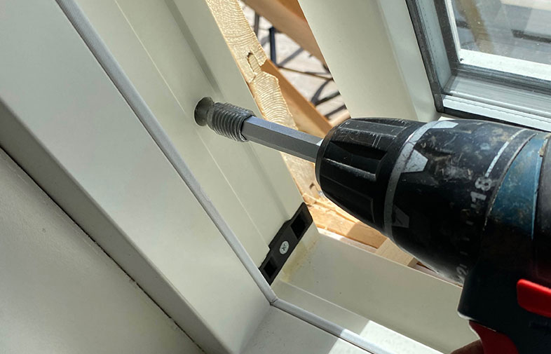 Blå-svart skruvdragare skruvar i vit fönsterkarm vid soligt fönster