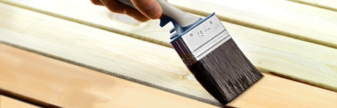 Hand med vit/grå pensel som stryker brun träolja på ljusa trallbrädor.