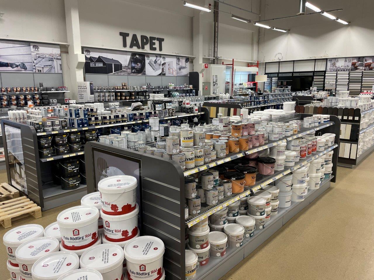 Butiksinteriör med rader av vita och färgade färgburkar på hyllor under skylten "TAPET".