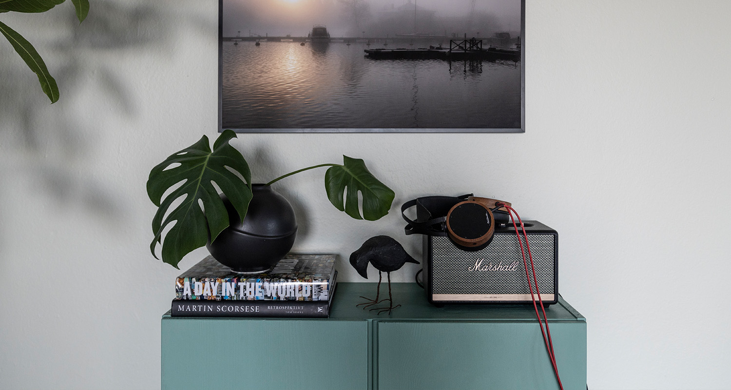 Turkos skåp med svart vas och grön monstera på böcker, Marshall-högtalare med träheadset