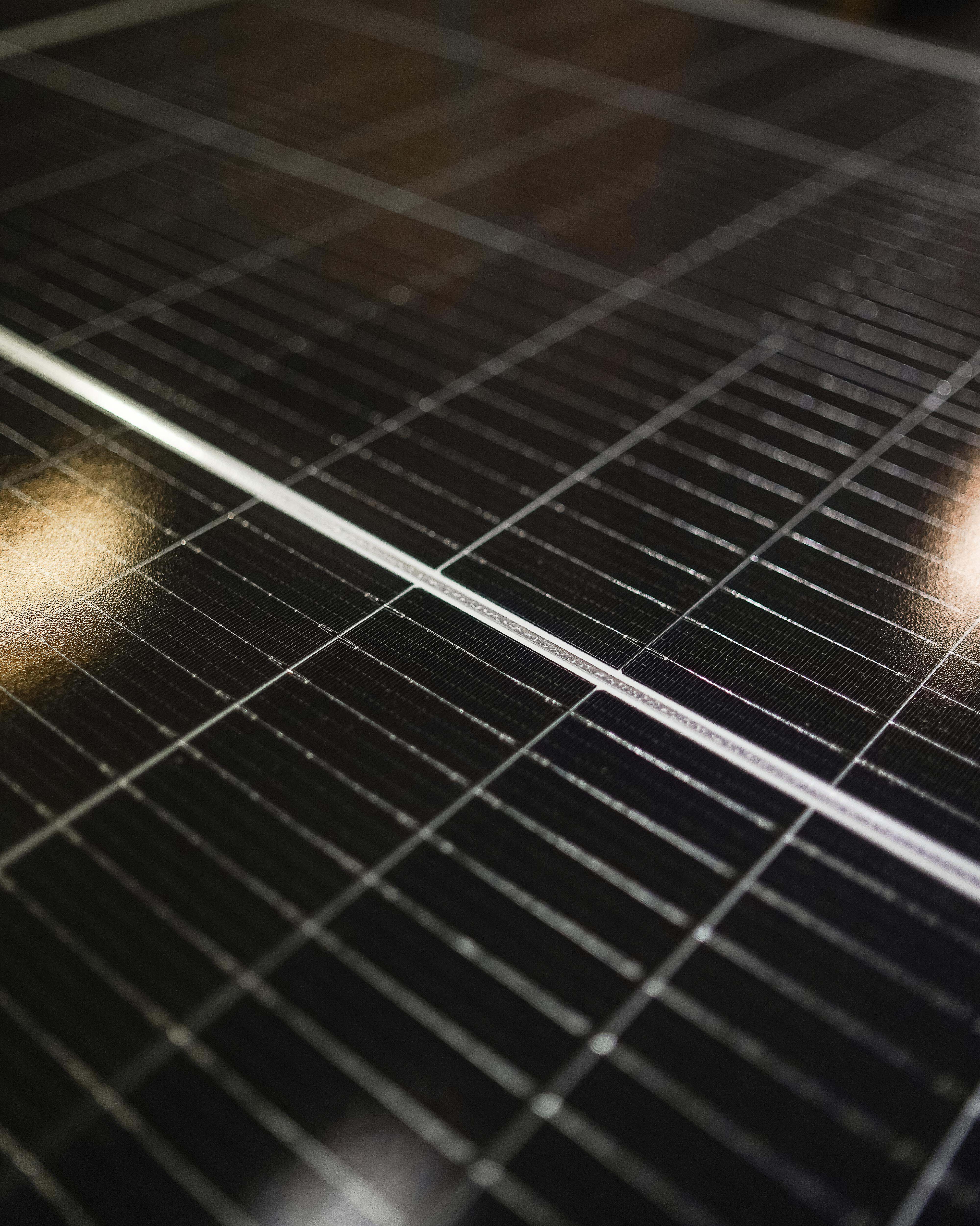 Närbild på mörka solcellspaneler med rutmönster och ljusreflexer.