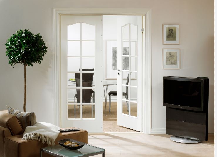 Ljust vardagsrum med brun skinnsoffa, grön krukväxt, vita glasdörrar mot matsal och svart TV.