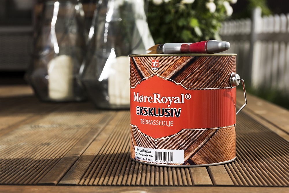 Röd burk "MøreRoyal Eksklusiv Terrassolja" med pensel på brunt trädäck.