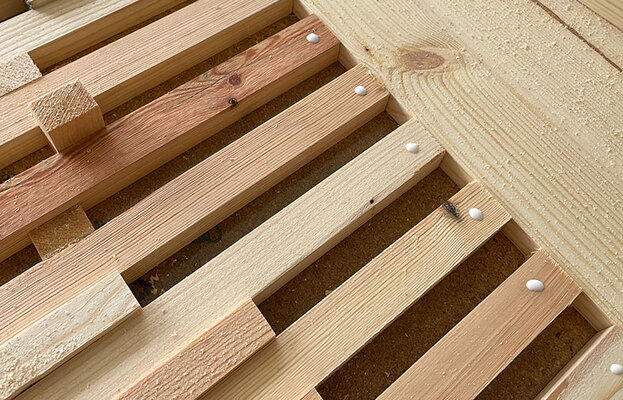 Närbild på parallella ljusa träslatsar med vita limdroppar och sågspån i hörnet.