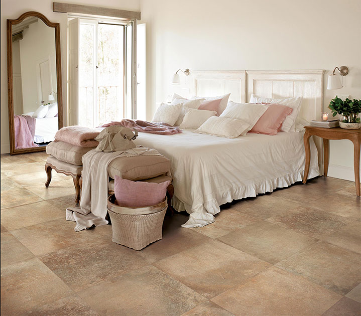 Soligt sovrum med vit säng, rosa kuddar, beige golv, antik spegel och grön växt