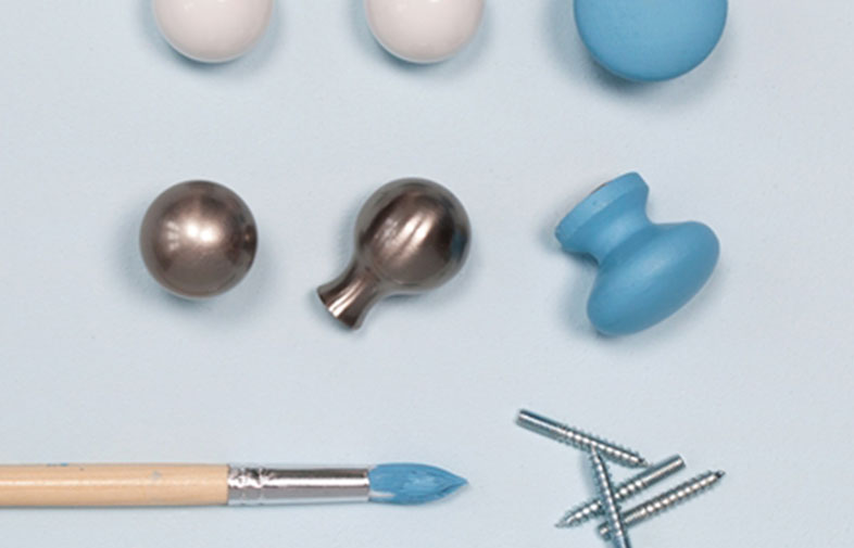 Vita och blå möbelknoppar, metallkulor, blå penselspets och skruvar på ljusblå bakgrund.