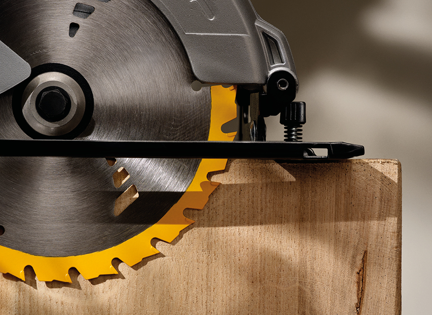 Närbild på metallisk cirkelsåg med gula tänder som skär i träplanka.