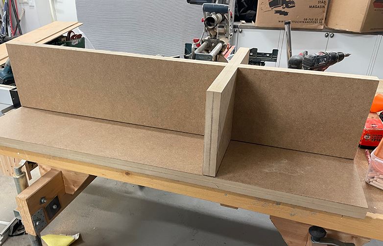 Bruna MDF-skivor sammanfogade till hyllsektion på träbänk i verkstad med verktyg i bakgrunden