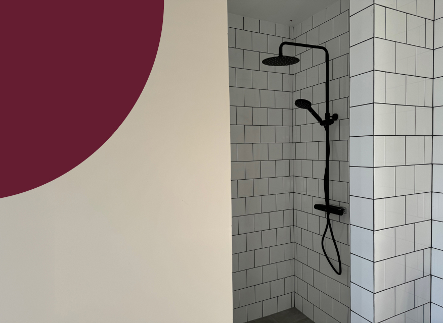 Vitt kaklat duschhörn med svart matt duschset, intill en beige vägg med vinröd cirkeldel.