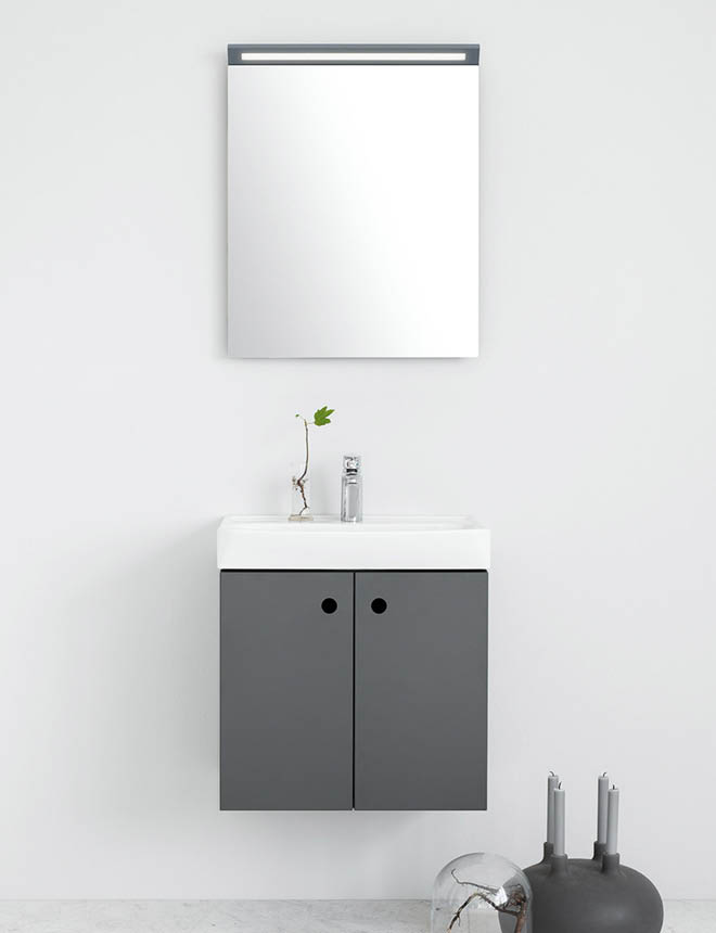 Vit vägg, grå kommod med vitt handfat, fyrkantig spegel, kvist i vas och grå ljusstake.