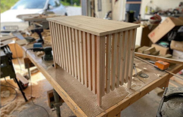 Ofärgad träkonsol med smala ribbor som ben på snickarbänk, verktyg i bakgrunden.