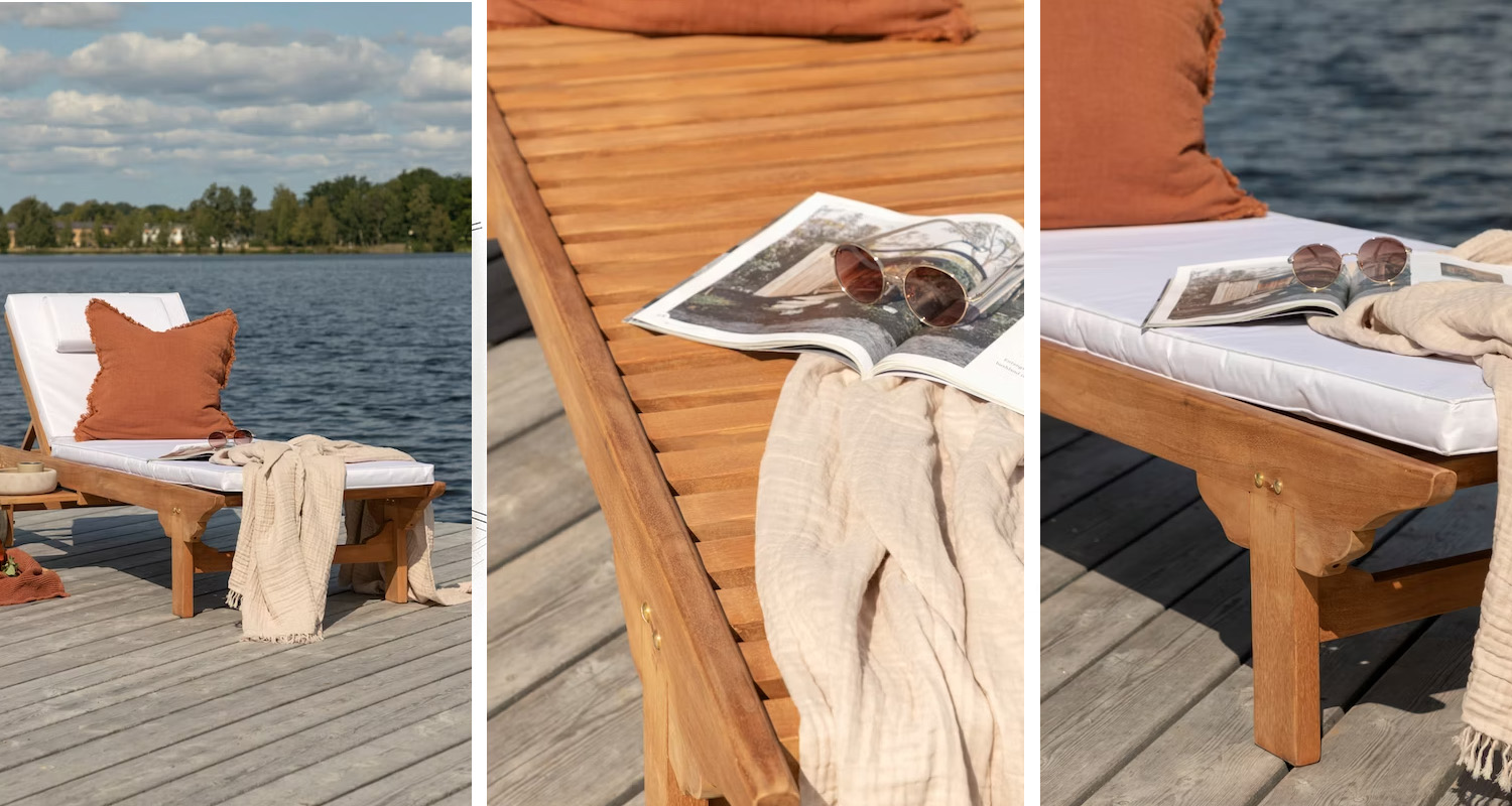 Träsolsäng på brygga vid sjö med vit dyna, rostorange kudde, beigen filt, solglasögon och tidning