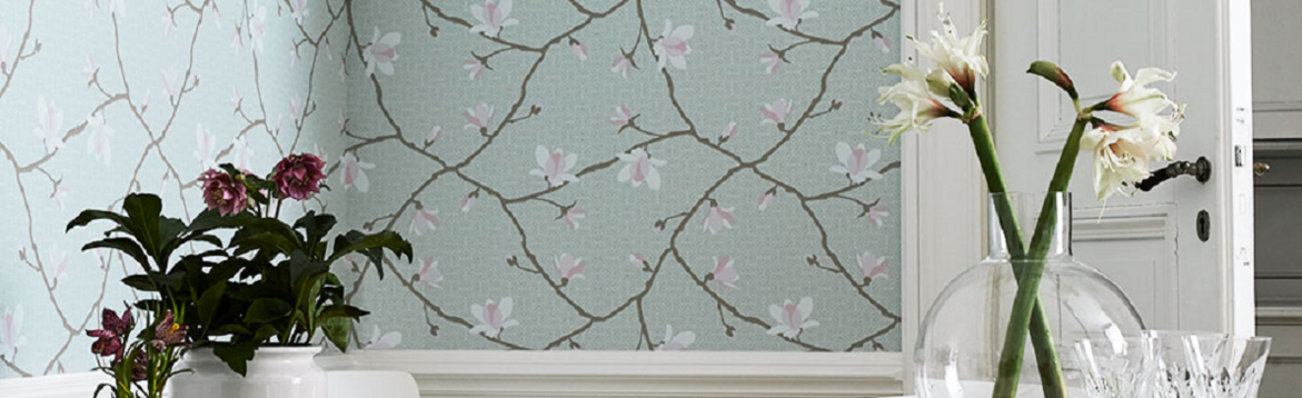 Alt-text (på svenska):  
Mintblå tapet med rosa magnoliakvistar, mörklila blommor i vit kruka och vita i glasvas.
