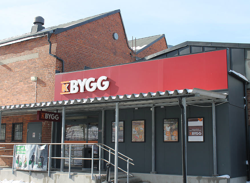 K-Bygg-butikens entré med röd fasad, K-Bygg-skylt och skyltfönster.
