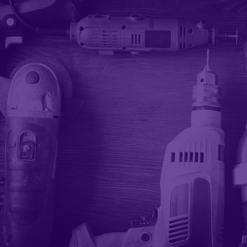 Lila tonade elverktyg – borrmaskin, vinkelslip och multiverktyg liggande på träbord.