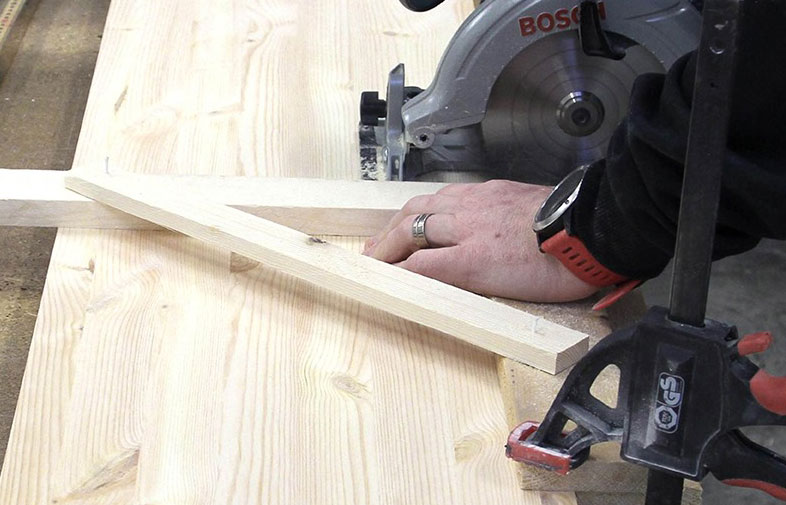 Grå Bosch-cirkelsåg skär ljust trä medan hand med röd armbandsklocka håller trästycke