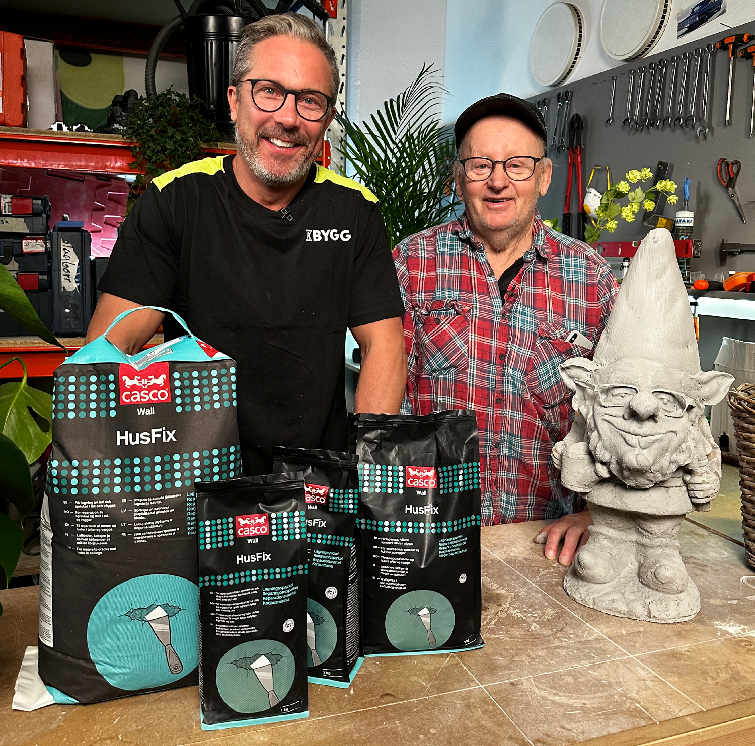 Två män i verkstad bakom bord med svarta och turkosa Casco HusFix-påsar samt betongtomte.