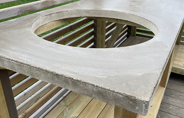 Grå betongskiva med cirkelformat hål på ljust trädäck utomhus.