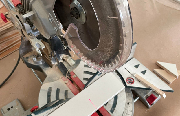 Grå kap- och geringssåg med roterande sågblad, röd laserlinje och vit trälist i verkstad