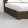 A close-up of a modern wooden bed frame with a white mattress and pillows, set on a light gray floor against a plain white wall.