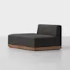 A modern armless sectional sofa with a dark charcoal cushion and a low wooden base, placed on a light-colored floor against a plain white background.